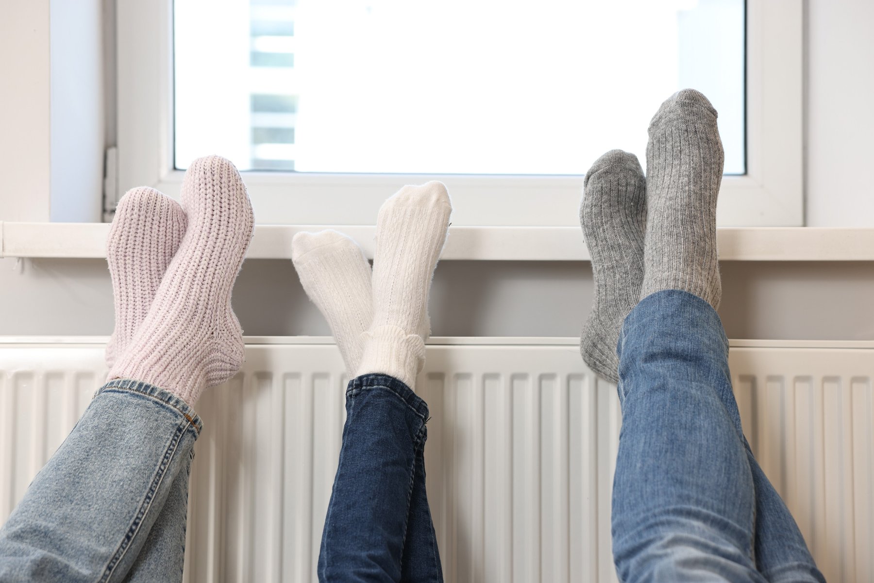 Three pairs of socked feet resting on a warm radiator